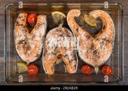 Gebackene Lachssteaks in Glasform mit Zitrone und Tomaten. Draufsicht. Stockfoto