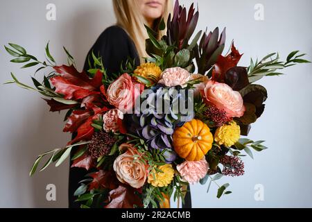 Reichhaltiger Blumenstrauß mit Herbstblumen und Kürbis in den Händen eines Mädchens. Heller Blumenstrauß. Ein Weihnachtsgeschenk. Wunderschöne Herbstblumen. Florist sammelte einen Strauß Stockfoto