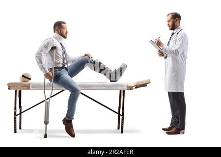 Ein Mann mit orthopädischem Stiefel und Halskragen sitzt auf einem Therapietisch und Physiotherapeut schreibt ein Dokument isoliert auf weißem Hintergrund Stockfoto