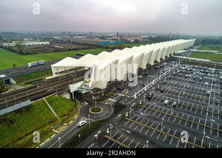 Luftaufnahme des Bahnhofs Reggio Emilia AV Mediopadana. Ein- und Ausstieg aus Zügen. Verkehr auf der Autobahn A1. Reggio Emilia, Emilia Romagna, Italien, Stockfoto