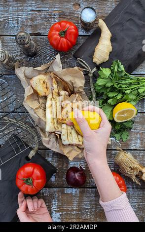 Die Hand einer Frau gießt Zitronensaft auf frisch gekochten Tintenfisch. Gegrillter Tintenfisch. Mediterrane Küche. Asiatische Küche. Stockfoto