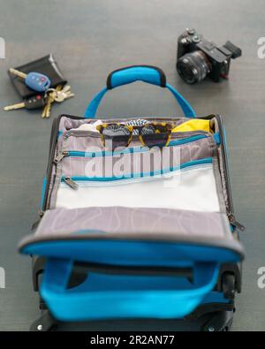 Kleine blaue Gepäcktasche mit Sonnenbrille, Kamera, Geldbörse und Schlüsseln für einen Urlaubsurlaub. Auf einem Betonboden. Stockfoto