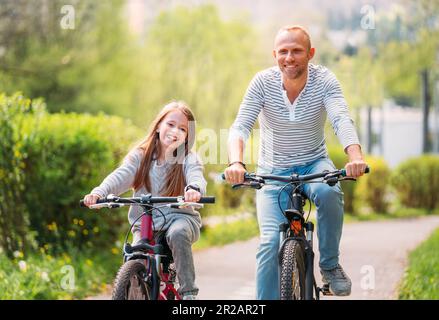 Porträts lächelnder Vater mit Tochter während des Sommerfahrens im Freien. Sie genießen die Zusammengehörigkeit im Sommer-Stadtpark. Glückliche Eltern und Chi Stockfoto