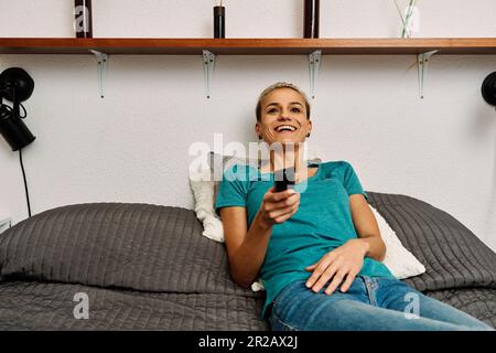 Glückliche Frau, die Fernsehen guckt, während sie auf dem Bett liegt Stockfoto