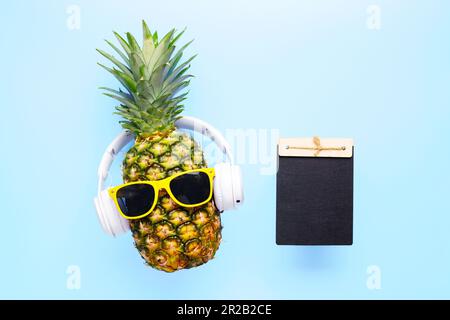 Ananas in Sonnenbrille mit leerer Tafel für Ihren Text auf blauem Hintergrund Stockfoto