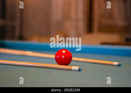 Roter Billardball mit Stichwort liegt auf einem grünen Billardtisch, Nahaufnahme. Billard Billardtisch im Retro-Stil Stockfoto