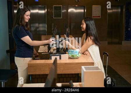 Frau bezahlt kontaktlos mit einem Smartphone an der Rezeption Stockfoto