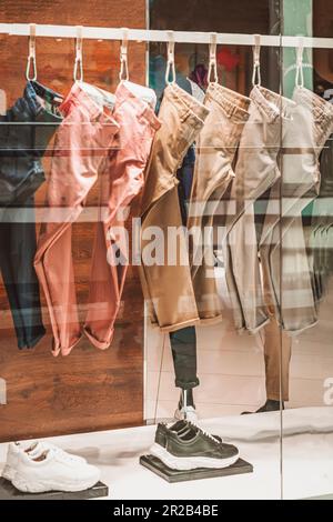 Mehrfarbige Herrenhosen, Kleiderbügel im Geschäft, Schaufenster, selektiver Fokus. Einkaufskonzept Stockfoto