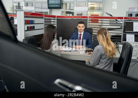 LGBT weibliches Paar und Leiter des Autohauses kommunizieren im Bürobereich Stockfoto