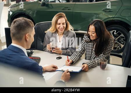 Eine charmante Asiatin unterschreibt einen Vertrag über den Kauf eines Autos Stockfoto