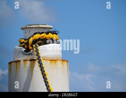 Großer weißer Anlegestapel mit leuchtend gelbem und schwarzem Seil zum Anbinden. Stockfoto