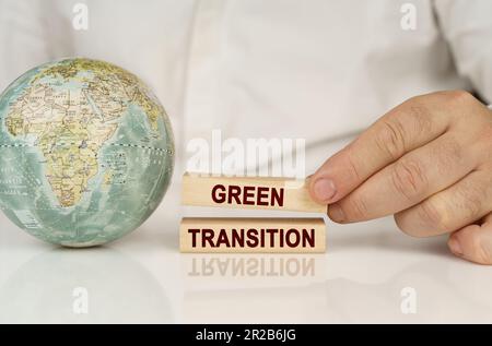 Auf einer weißen reflektierenden Oberfläche befindet sich ein Globus in den Händen von Holzblöcken mit der Aufschrift „Grüner Übergang“. Das Konzept von Industrie und Umwelt Stockfoto