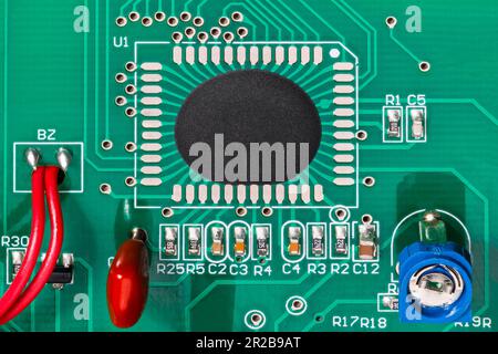 Chip-on-Board-Baugruppe eines integrierten Schaltkreises auf einer Leiterplatte mit grüner Textur und roten Drähten. Microchip in Epoxidharz-Tropfen und elektronischen Bauteilen. Potentiometer. Stockfoto