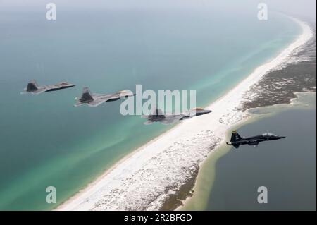 USA Air Force F-22 Raptors, die der 43D. Kampfgeschwader zugeteilt wurden, und ein T-38A Talon, die der 2D. Kampfgeschwader zugeteilt wurden, fliegen eine unterschiedliche Formation über dem Florida Panhandle, 10. April 2023. Die Formation war eine Hommage an die frühere Mission des 325. Fighter Wing, F-22 Raptor-Piloten fast 20 Jahre lang auszubilden. Der Flügel geht auf eine Kampfmission über, mit F-35A Lightning II Kampfflugzeuge, die in den nächsten Jahren ankommen. (USA Air Force Foto von Tech. Sgt. Betty R. Chevalier) Stockfoto