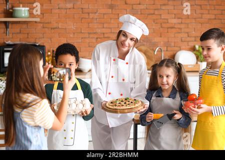 Ein kleines Mädchen, das nach dem Kochkurs in der Küche ein Foto von einer Chefköchin mit zubereiteter Pizza macht Stockfoto