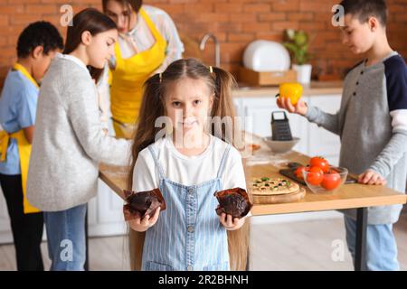 Kleines Mädchen mit zubereiteten Muffins nach dem Kochkurs in der Küche Stockfoto