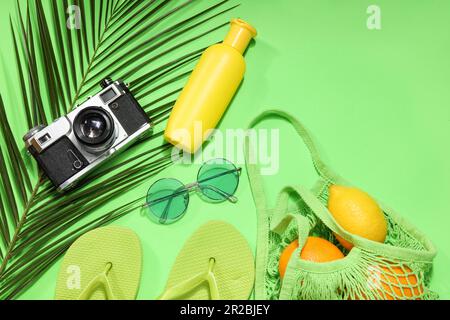 Schnürtasche mit Früchten, Strandzubehör und Palmenblatt auf grünem Hintergrund Stockfoto