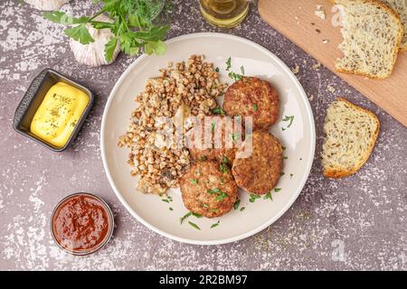 Koteletts mit Buchweizen, Pilze und Petersilie auf grauem Grunge-Tisch in der Küche Stockfoto