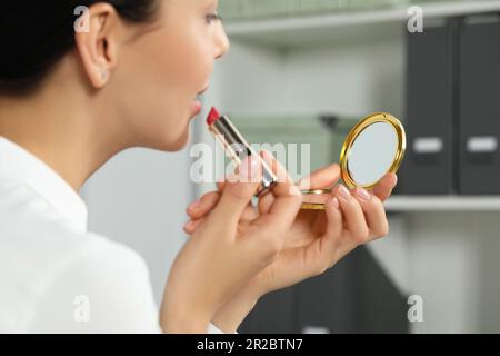 Eine junge Frau, die einen Kosmetikspiegel benutzt, während sie sich schminkt, Nahaufnahme Stockfoto