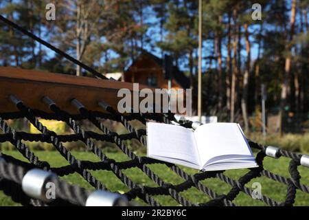 Komfortable NetzHängematte mit offenem Buch im Freien an sonnigen Tagen Stockfoto