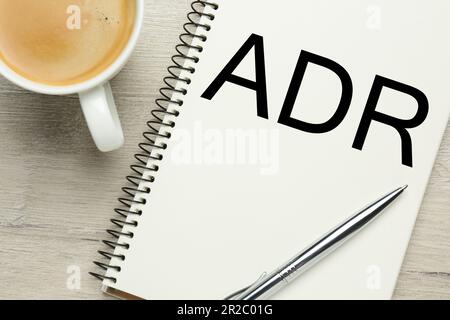 Alternative Streitbeilegung. Notizbuch mit Abkürzung ADR, Stift und Tasse Kaffee auf Holztisch, flach liegend Stockfoto