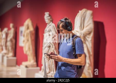 Porträt eines zeitgenössischen Mannes, der sich Skulpturen ansieht und Audioguide auf der Museumsausstellung hört Stockfoto