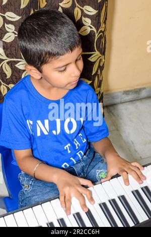 Asiatischer Junge, der Synthesizer oder Klavier spielt. Süßes kleines Kind, das Klavier lernt. Kinderhände auf der Tastatur im Haus Stockfoto