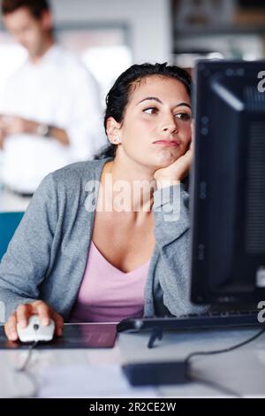 Ich brauche einen neuen Job... Eine gelangweilte junge Geschäftsfrau, die auf ihren Computerbildschirm starrt. Stockfoto