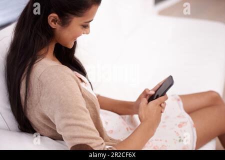Senden einer Kurznachricht. Eine junge Frau, die zu Hause sitzt und ihr SMS auf ihrem Handy schreibt. Stockfoto