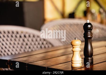 Szene mit Salz- und Pfefferstreuern aus Holz, Mühlen auf einem rustikalen Holztisch vor der Kulisse eines Restaurants. Stockfoto