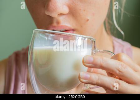 Ein junges ukrainisches Mädchen hält morgens einen durchsichtigen Glasbecher mit Milch Stockfoto