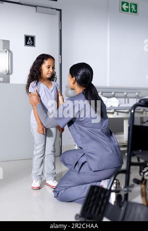 Kniende, birassische Ärztin und weibliche Patientin, die im Krankenhausflur spricht Stockfoto