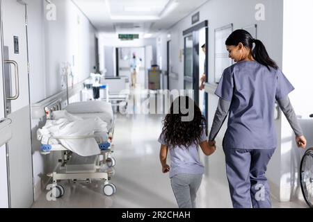 Lächelnde, birassische Ärztin und Patientin, die sich im Krankenhausflur die Hände hält Stockfoto