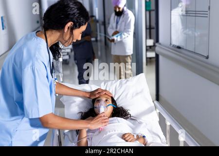 Birassische Ärztin, die im Krankenhauskorridor eine Sauerstoffmaske auf eine Patientin auflegt Stockfoto