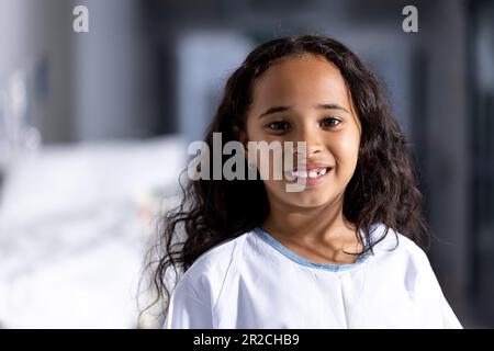 Porträt einer glücklichen, birassischen Patientin mit langen, lächelnden Haaren im Krankenhausgang Stockfoto