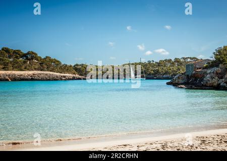 Cala S'Amarador Strand mit weißem Sand und türkisfarbenem Meer in der natürlichen Parklandschaft Cala Mondrago Bay auf Mallorca, Balearen, Spanien. Schwimmende Segelboote Stockfoto