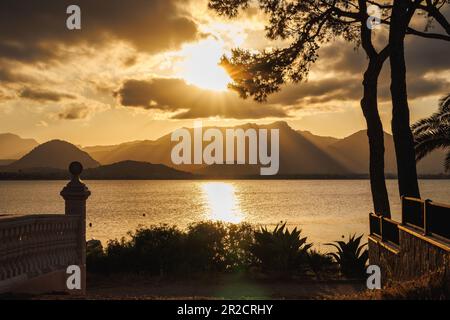 Sonnenuntergang über der Bucht von Pollenca, Mallorca. Der Sonnenstrahl scheint in goldener Stunde durch die Wolken. Touristenresort im wunderschönen Mallorca, Balearen, Spanien Stockfoto