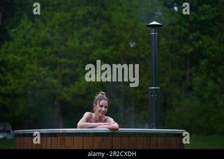 Junge, glückliche Frau, die sich im Whirlpool entspannt. Genießen Sie das Wellness-SPA im Freien in den Wäldern. Heißes Bad MIT WHIRLPOOL. Hochwertiges Foto Stockfoto