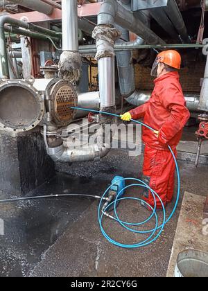 Man reinigt Kondensatorrohre, entfernt Kalkablagerungen des petrochemischen industriellen Wärmetauschers mit einer Hochdruck-Wasserstrahlmaschine Tragen Sie Helm und Stockfoto