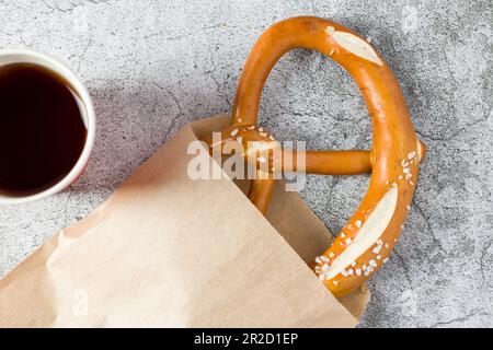 Brezel in Geschenkpapier eingewickelt mit einem Getränk daneben auf einem Steintisch Stockfoto