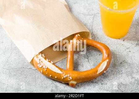 Brezel in Geschenkpapier eingewickelt mit einem Getränk daneben auf einem Steintisch Stockfoto