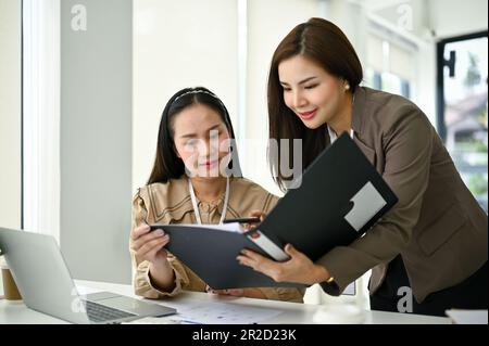 Eine wunderschöne junge asiatische Sekretärin, die Fragen zu einem neuen Projekt von ihrem Chef stellt, diskutiert und zusammenarbeitet. Stockfoto