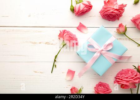 Hintergrund zum Valentinstag mit pinkfarbenen Rosen und Geschenkbox auf weißem Tisch. Draufsicht Stockfoto
