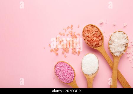 Verschiedene Arten von Wellnesssalz in Holzlöffeln auf rosa Hintergrund. Draufsicht Stockfoto