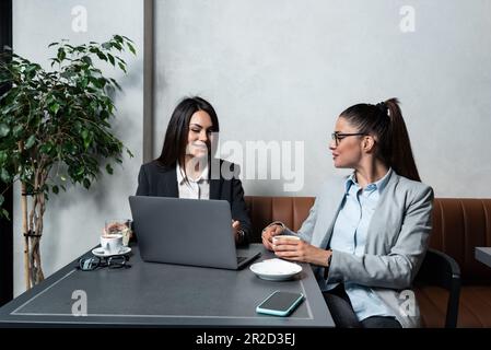 Zwei junge weibliche Geschäftspartner, Inhaber eines kleinen Unternehmens, neu auf dem Markt, eine Arbeitsunterbrechung in einem Café, reden und trinken Kaffee, machen pla Stockfoto