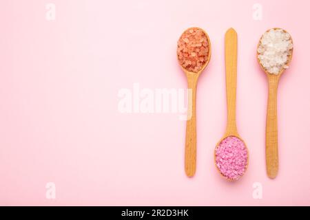 Verschiedene Arten von Wellnesssalz in Holzlöffeln auf rosa Hintergrund. Draufsicht Stockfoto