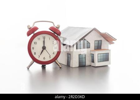Wecker und Hausmodell. Zeit für eine Hypotheken- oder Immobilienversicherung Stockfoto