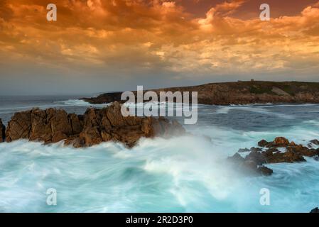 Wellen mit Seideneffekt bei Sonnenuntergang mit orangefarbenem Himmel auf den Klippen von Punta Herminia Stockfoto