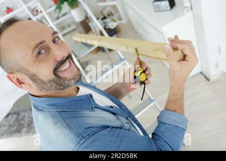 Ein Mann lacht, während er zu Hause Holz misst Stockfoto