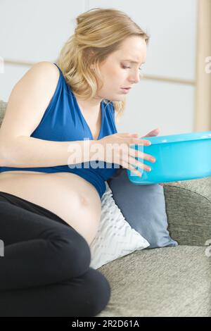 Schwangere Frau auf dem Sofa, die eine Plastikschüssel in der Hand hält Stockfoto